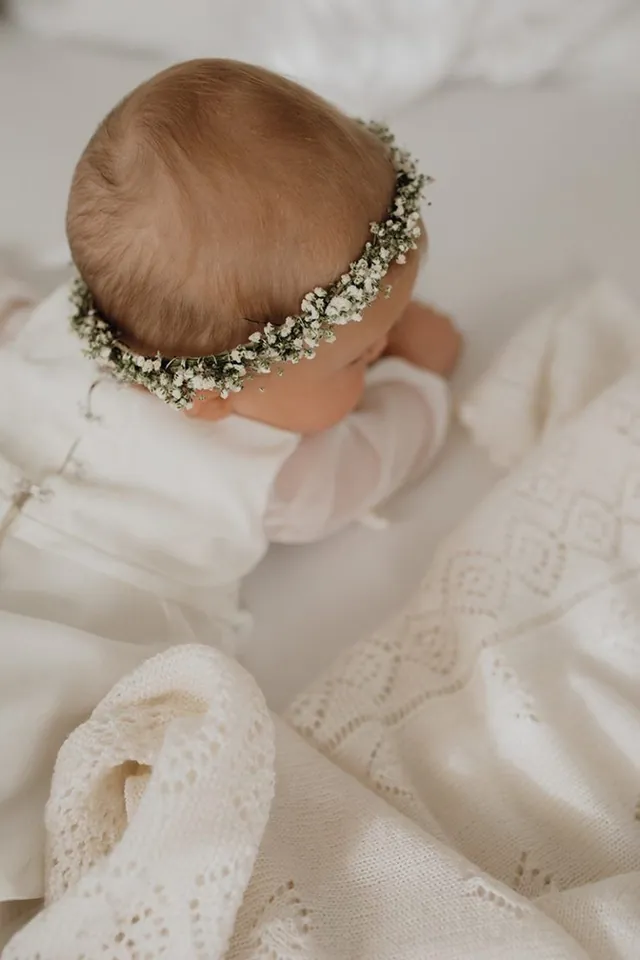 Schlafendes Baby mit Blumenkranz auf einer weissen Strickdecke.